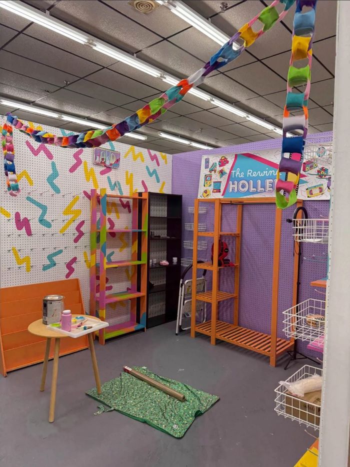 Booth B50 coming together: a white pegboard wall painted with bright 90s squiggles, a purple pegboard wall with The Rewind Holler banner, orange shelves, and a rainbow paper-chain garland overhead