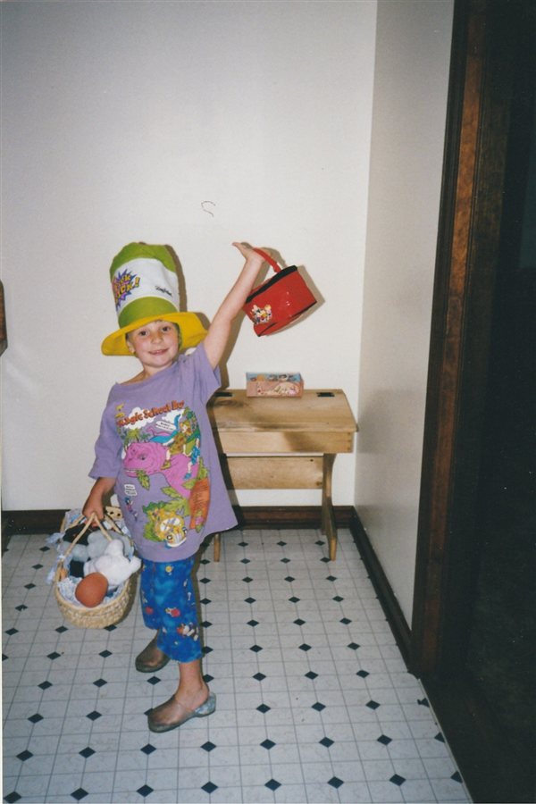 Hannah as a kid in a tower of stacked hats, mid dress-up chaos